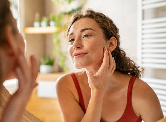 une femme heureuse regarde un teint clair dans un miroir