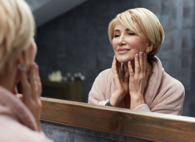 femme sourit à la réflexion dans le miroir de la salle de bain, peau éclatante