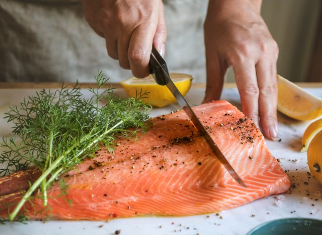 Personne coupant en tranches le saumon frais avec l'aneth et le citron
